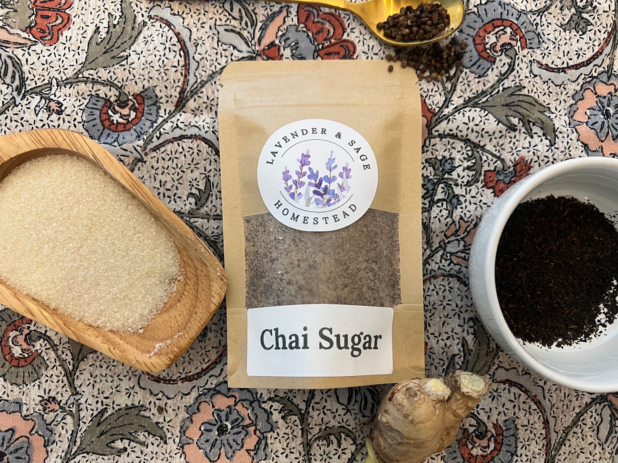 Package of Chai Sugar surrounded by black tea, ginger, cardamom, and sugar